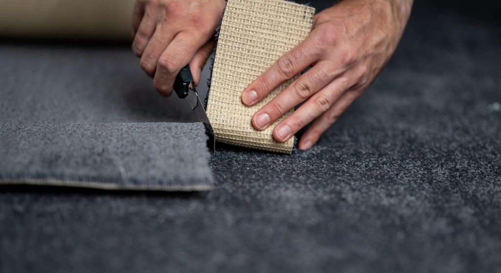 Carpet fitter trimming grey carpet with a utility knife